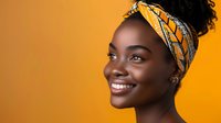 Young African woman with bright smile wearing colorful yellow and blue headwrap against vibrant orange background, radiating joy and confidence.
