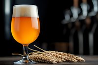 Glass of unfiltered craft beer with white foamy head and fresh wheat ears on dark wooden table, selective focus on amber liquid against blurred bar.