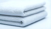 Stack of clean white folded terry towels on light background, conveying freshness, hygiene, and comfort for spa, hotel, or bathroom concepts.