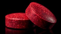 Red compressed tablets or pills against black background with reflective surface, pharmaceutical or supplement product photography.