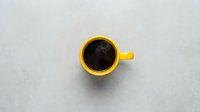 Yellow coffee mug with black coffee on white marble surface, top view flat lay for morning beverage concepts and cafe branding materials.