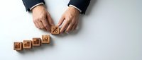 Businessman hands protecting wooden blocks with house icons representing real estate investment portfolio growth and property management strategy.