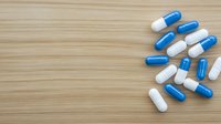 Blue and white medical capsules scattered on wooden surface with copy space for pharmaceutical or healthcare messaging. Overhead view on natural wood background.