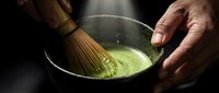 Matcha whisk blending vibrant green tea powder in ceramic bowl, traditional Japanese tea ceremony preparation for culinary and wellness content.