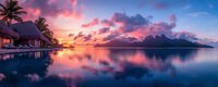 Panoramic view of overwater bungalows at sunset with dramatic pink clouds reflecting in calm lagoon waters, silhouetted palm trees and mountain peaks on horizon.