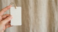 Blank white price tag held in hand against neutral fabric background for branding, labeling, and retail product mockup purposes.