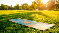 Yoga mat placed on lush green grass in sunny park setting, ideal for wellness, fitness, and outdoor exercise marketing materials.