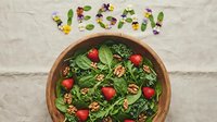 Fresh vegan salad with spinach, kale, strawberries, and walnuts in wooden bowl, with word vegan made of greens and edible flowers.