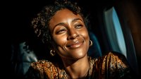 Happy African American woman with curly hair smiling warmly in golden lighting, expressing joy and positivity for lifestyle and wellness content.