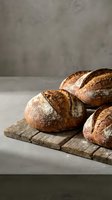 Freshly baked artisan bread loaves with golden crust on rustic wooden cutting board against neutral background for bakery and food photography.