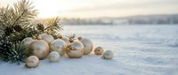 Champagne and gold ornaments with evergreen branches arranged on snow, winter holiday decoration with blurred frozen landscape background.