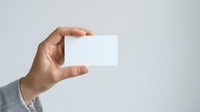 Male hand holding blank white business card against neutral background, suitable for branding, corporate identity, and marketing mockup designs.