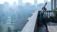 Woman stretching on rooftop terrace overlooking city skyline. Wellness, fitness, and urban lifestyle concept for health and mindfulness content.
