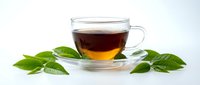 Glass cup of black tea with fresh green leaves on white background isolated for healthy beverage design and wellness marketing materials.