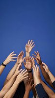 Diverse group of hands reaching upward against bright blue sky representing unity, teamwork, volunteering and community support concepts.