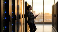 Professional businesswoman using smartphone in modern data center server room during golden hour sunset for technology and communication concepts.