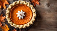 Fresh baked pumpkin pie with whipped cream rosette topping on rustic wooden background with autumn oak leaves, traditional Thanksgiving dessert.