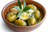 Fresh marinated green olives with herbs and olive oil in rustic ceramic bowl, garnished with fresh olive leaves, close up view on white background.
