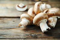 Fresh white champignon mushrooms scattered on rustic wooden table with natural lighting, macro food photography for restaurant menu and cooking blogs.