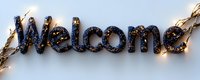 Glowing welcome sign with black glitter text illuminated by warm LED string lights against white background, creating welcoming atmosphere for hospitality business.