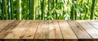 Wooden table surface with blurred green bamboo forest background, suitable for product display and nature-themed designs.