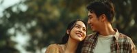 Young Asian couple sharing intimate moment outdoors in warm golden light, woman leaning against man's shoulder, both smiling happily in casual autumn clothing.