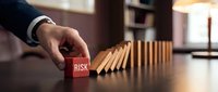 Businessman hand stopping falling dominoes with red risk block, symbolizing crisis management and financial protection strategy.