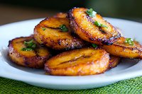 Grilled sweet plantains with caramelized edges and fresh herbs served on white plate, showcasing traditional Caribbean cooking technique and garnished with cilantro.