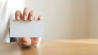 Woman holding blank white business card with manicured nails, ideal for corporate branding and professional networking presentations.