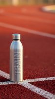 Stainless steel water bottle with engraved text positioned on red athletic track surface with white lane markings, ideal for sports and fitness marketing.