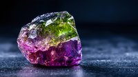 Raw watermelon tourmaline crystal with vibrant pink and green colors on dark background shows natural mineral formation with dramatic lighting effects.