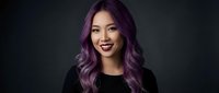 Young Asian woman with vibrant purple hair and dark lipstick smiling confidently against black background for beauty and fashion projects.