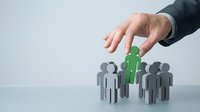 Male hand in business suit selecting green figure among gray figures, representing recruitment, hiring, talent selection, and human resources management concept.