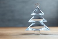 Elegant crystal Christmas tree ornament on wooden surface against blurred gray background, perfect for holiday decor.