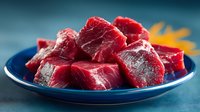 Fresh raw beef chunks cut into cubes on blue plate ready for cooking stew or roast. High protein red meat ingredient for healthy meal preparation.