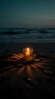 Glowing candle in glass holder on sandy beach at twilight with ocean waves and starry sky creating peaceful atmosphere for meditation and relaxation.