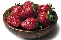 Fresh ripe strawberries with green leaves in rustic wooden bowl against white background, macro food photography for healthy eating and recipe designs.