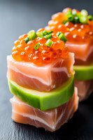Fresh salmon and avocado bites topped with red caviar and green onions on black slate background. Elegant Japanese fusion appetizer for luxury catering.