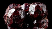 Deep red garnet crystal cluster with lustrous faceted surfaces and natural mineral formation displaying rich burgundy coloration against dark background.