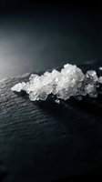 Coarse sea salt crystals scattered on dark slate surface with dramatic lighting for culinary and cooking applications.