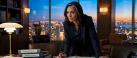 Professional businesswoman in dark suit leaning on desk in modern office with city skyline view at dusk. Corporate executive leadership concept for business presentations.