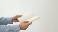 Male hands in light blue shirt sleeves holding open blank book with white pages against neutral background for reading and education concepts.