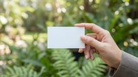 Hand holding blank white business card outdoors with lush green bokeh garden background, mockup template for branding and identity design.