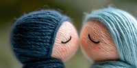 Romantic close up of two knitted dolls with yarn hair in navy blue and mint green colors kissing against blurred background, sweet tender moment.