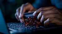 African American male hands typing on illuminated keyboard with glowing red digital particles effect representing cybersecurity, data transfer or coding work.