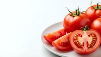 Fresh ripe red tomatoes whole and sliced on white plate against clean background for healthy cooking and food preparation concepts.