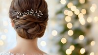 Elegant bridal updo hairstyle with crystal hair accessories against blurred holiday lights background, showcasing intricate twisted bun and delicate hair pins.