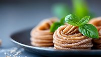 Fresh whole wheat pasta nests garnished with pecan nuts and green basil leaves on dark plate, selective focus with copy space for menu design.