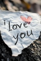 Handwritten I love you message with red heart on crumpled white paper lying on rocky ground for romantic greeting cards and Valentine's Day designs.