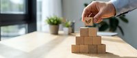 Businessman hand placing wooden cube with checkmark on pyramid stack for goal achievement and success planning in modern office environment.